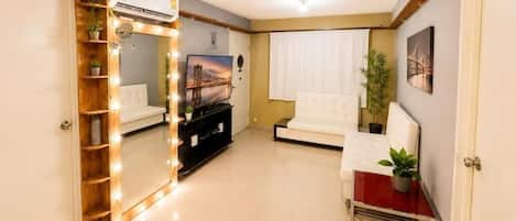 A living room with a vanity mirror, a sofa, a television, and a small table with a plant.