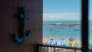 Vista al mar desde una ventana con detalles de madera y barandilla metálica.