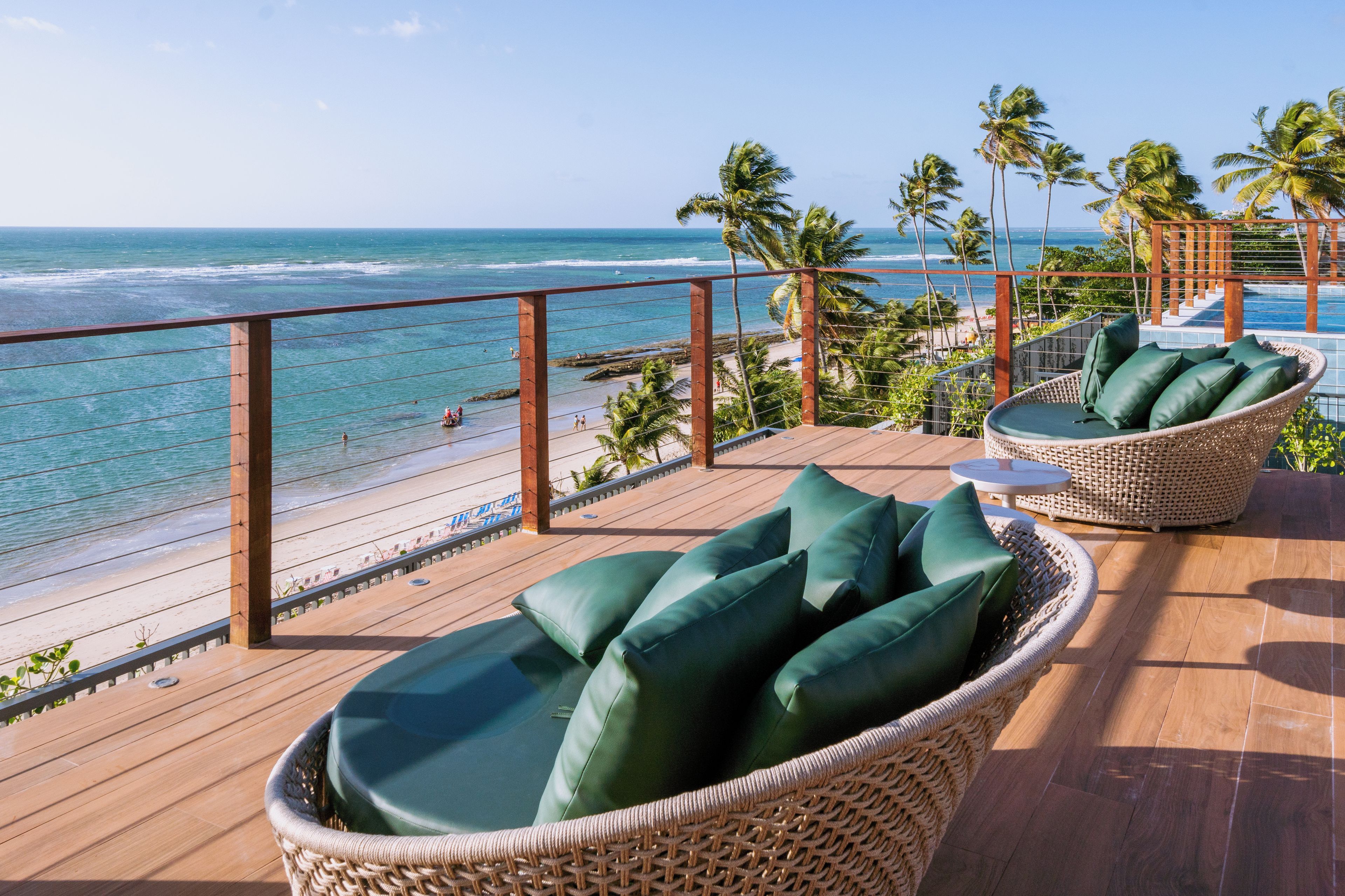 A deck with wicker furniture and a view of the beach and ocean.
