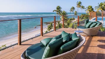 A deck with wicker furniture and a view of the beach and ocean.