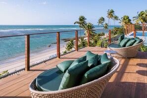 A deck with wicker furniture and a view of the beach and ocean.