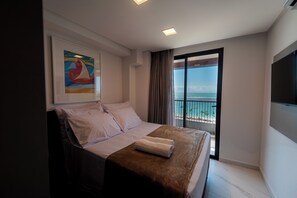 A hotel room with a bed, a painting, a window with a view of the sea, and a flat-screen TV. - Smeralda del Mare by AFT (Ipojuca)