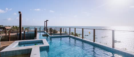 A pool with a view of the sea, surrounded by a wooden deck and a metal railing.