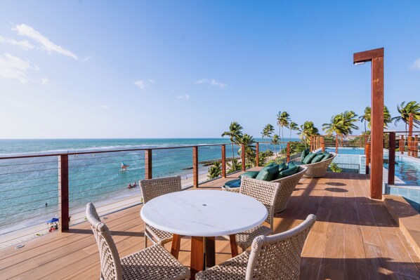 A deck with a table and wicker chairs overlooking a beach and ocean.