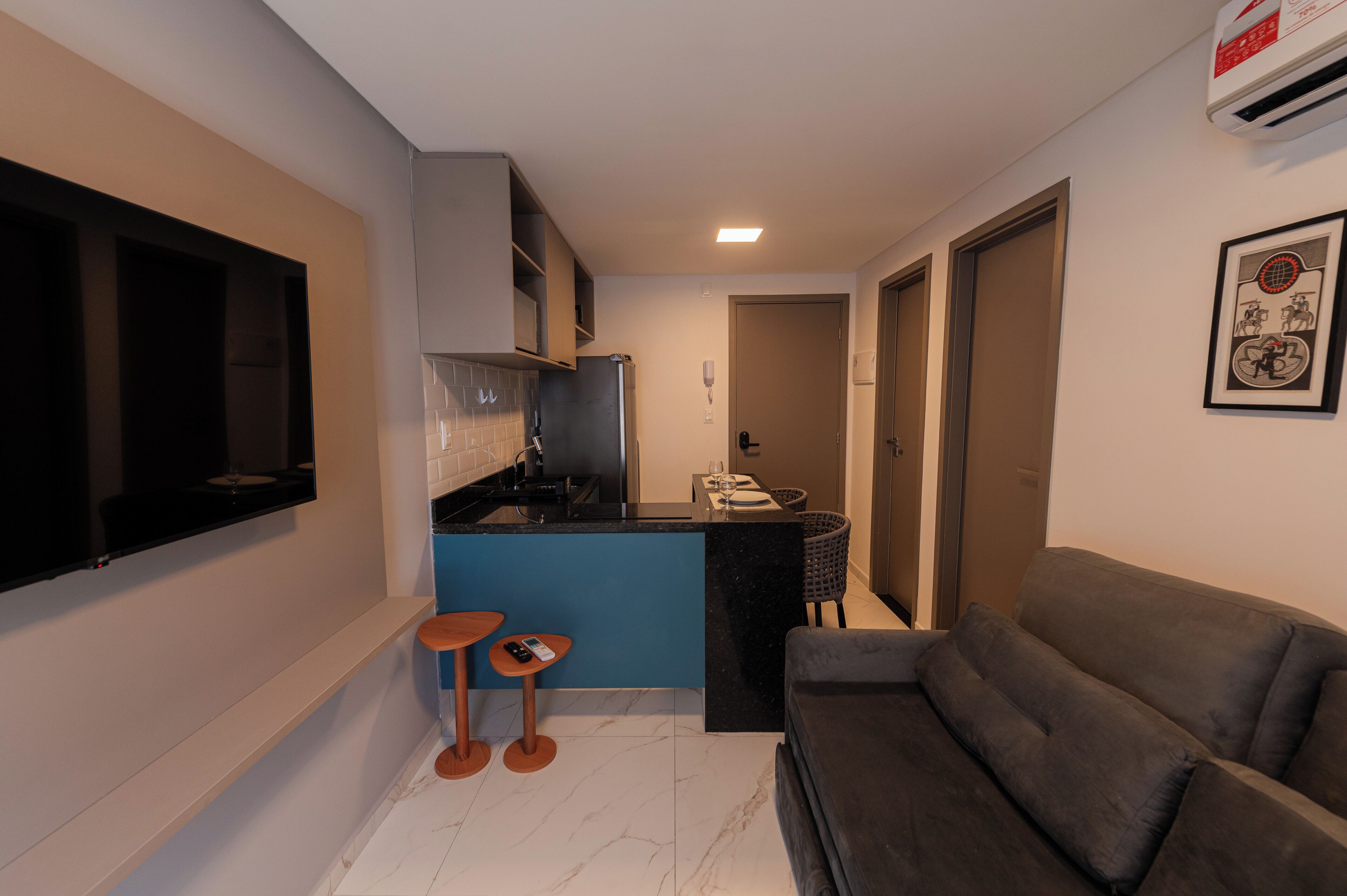 A compact living space with a kitchenette, a flat-screen TV mounted on the wall, a sofa, and a small dining area.