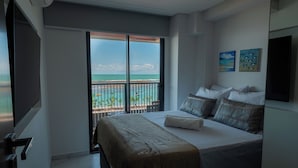 Habitación de hotel con cama, televisión, balcón con vista al mar y dos cuadros en la pared.