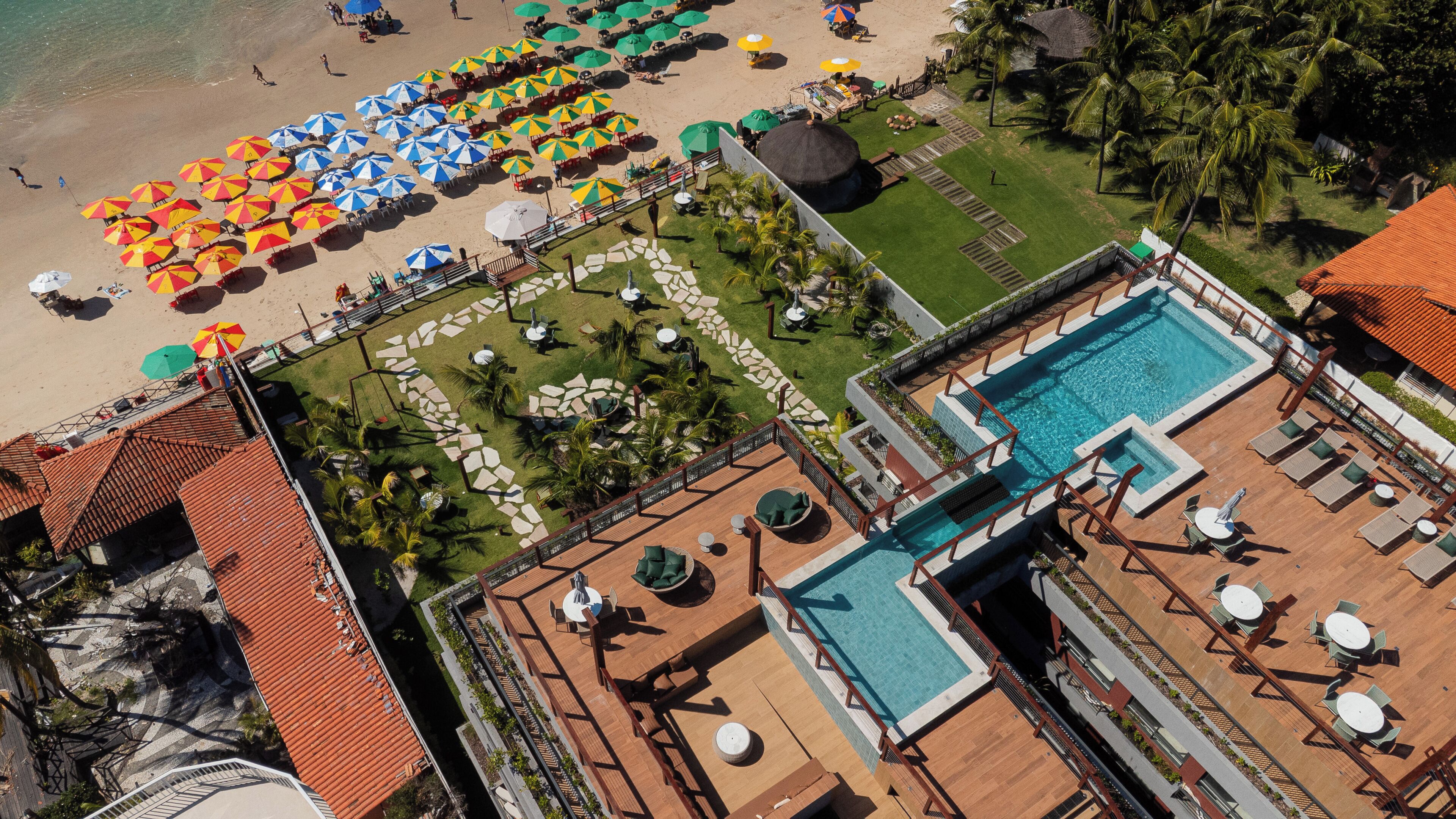 An aerial view of a resort with a swimming pool, beach umbrellas, and a well-maintained lawn.