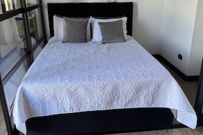 A bed with a patterned bedspread and two pillows, a black headboard, and a glass door leading to a balcony. - EON Zone 10. Luxury, views, and comfort—all in one apartment. (Ciudad de Guatemala)