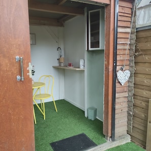 A small room with a green artificial turf floor, a yellow chair, a white shelf with a kettle, and a heart-shaped decoration.