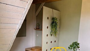 A room with a sloped ceiling, a wooden bench, a round yellow table with matching chairs, and a potted plant on the table.