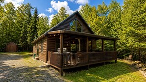 Eine Holzhütte mit einer überdachten Veranda, einem kleinen Schuppen und bewaldeter Umgebung.