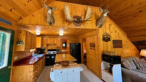 Ein Innenraum einer Holzhütte mit Holzwänden, einer Küchenzeile, einem Esstisch und einer Couch.