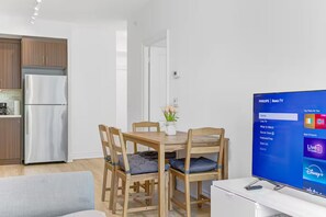 Un espace de vie moderne comprenant un coin repas, une cuisine et un téléviseur affichant l’interface Roku TV.