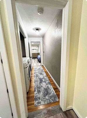 A narrow hallway with a washing machine, a rug, and a door leading to another room.