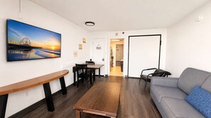 A modern living room with a sofa, a dining table, and chairs. There is a painting on the wall and a door leading to another room. - Oceanfront 7th-Floor Escape | Pool (Myrtle Beach)