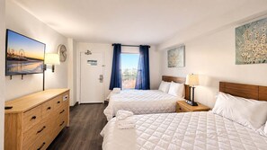 A hotel room with two beds, a wooden dresser, a desk, a clock, and a painting on the wall. - Oceanfront 7th-Floor Escape | Pool (Myrtle Beach)