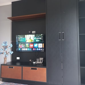 A modern entertainment unit with a flat-screen TV displaying various channels and a decorative vase with blue flowers.