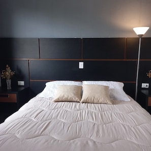 A hotel room with a large bed, two bedside tables, a nightstand, a lamp, and a vase with dried flowers.