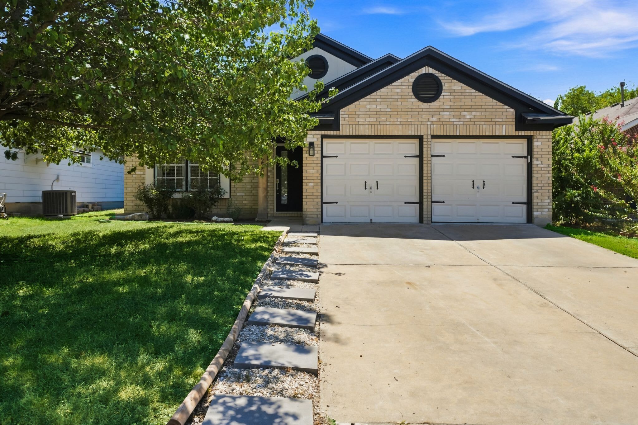 Un garage attenant à une maison, avec deux portes blanches, une façade en briques et un ciel dégagé.