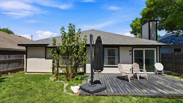 Un patio trasero residencial con terraza de madera, un espacio cubierto de patio y un pequeño árbol.