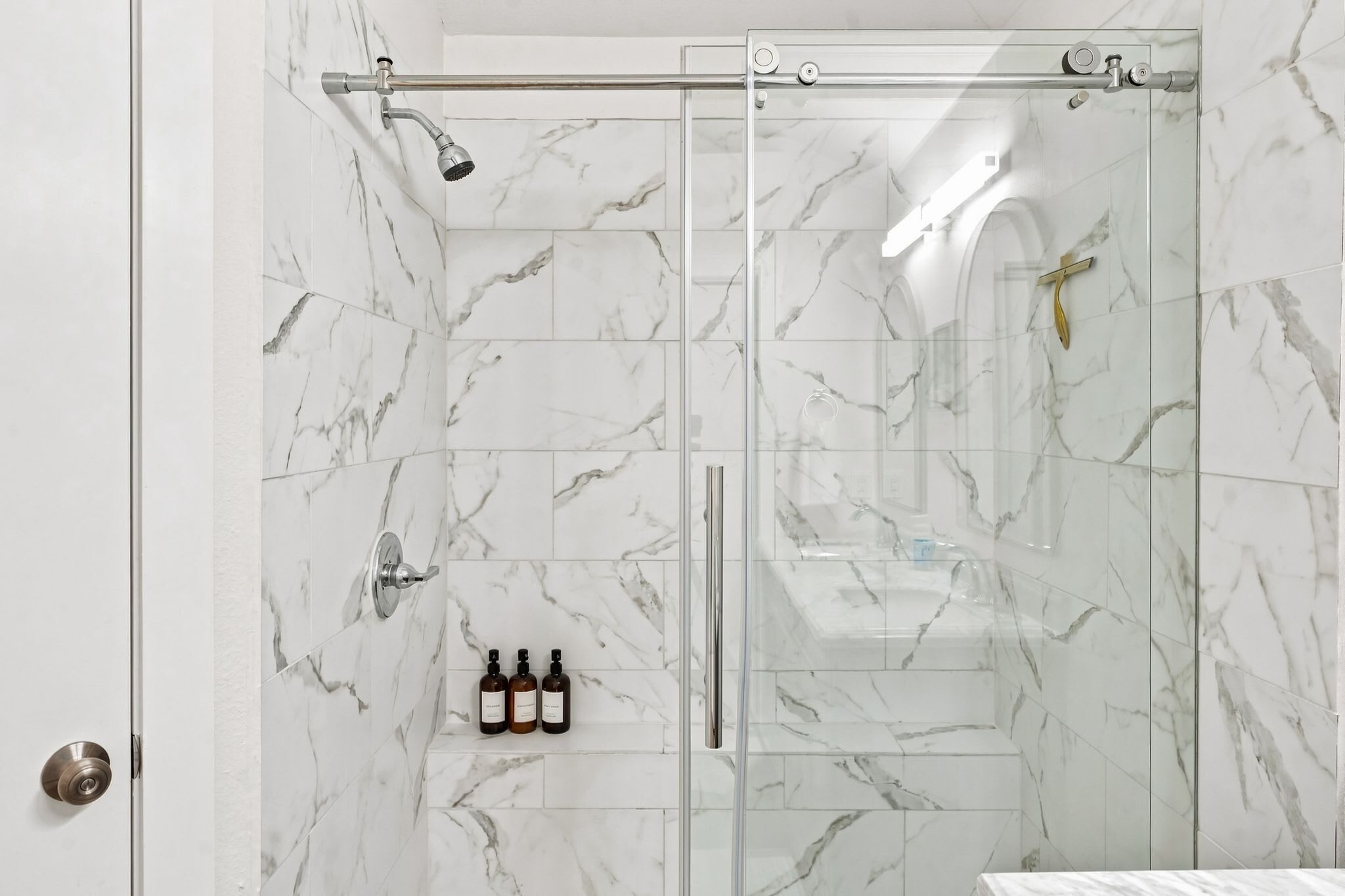 A glass-enclosed shower with marble tiles and a handheld showerhead.
