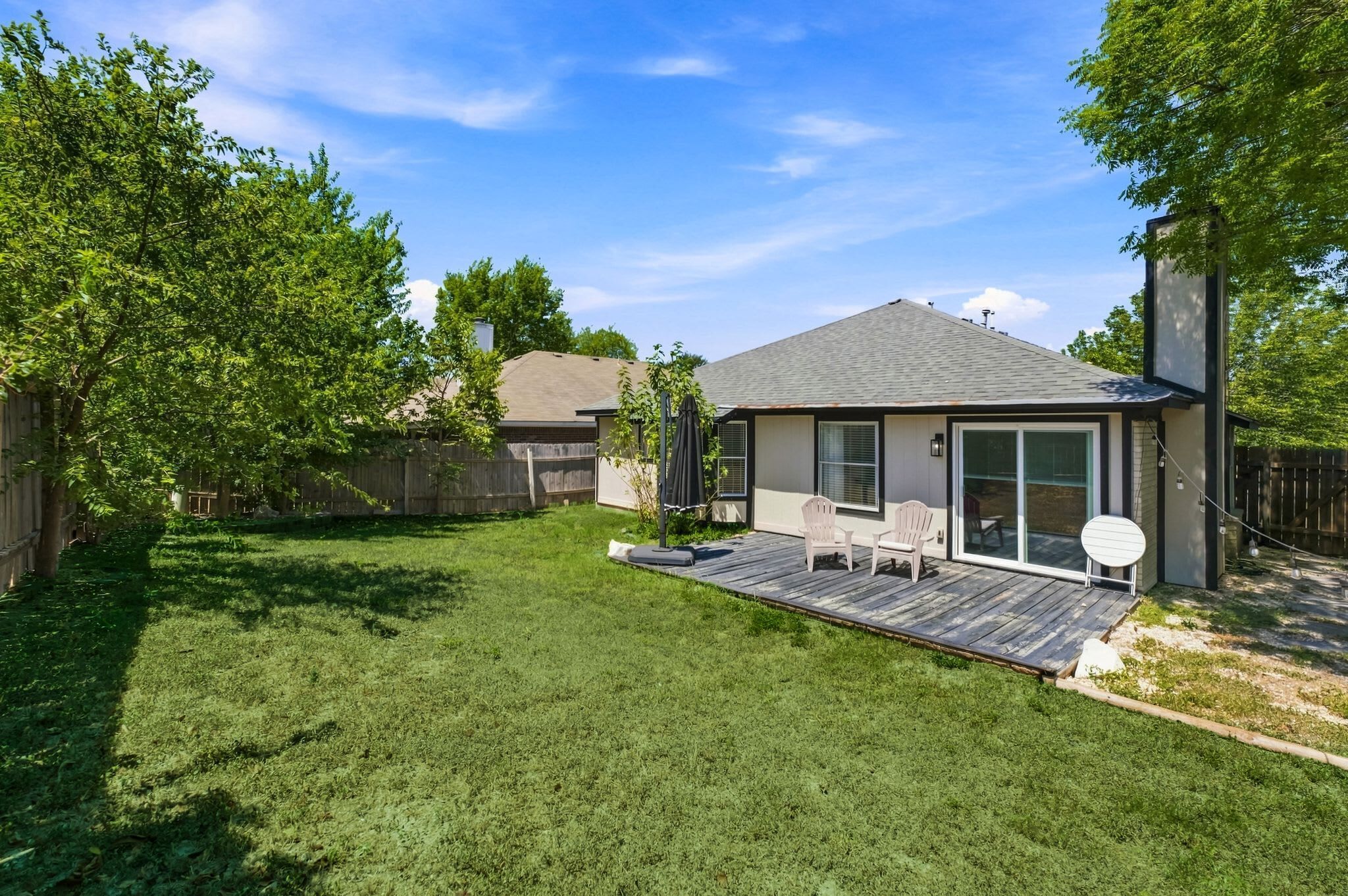 A backyard with a patio, a covered seating area, and a house with a garage.