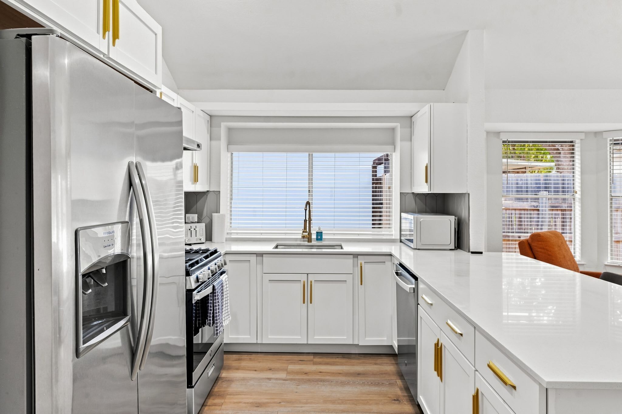 A modern kitchen with white cabinetry, stainless steel appliances, and a window with blinds.