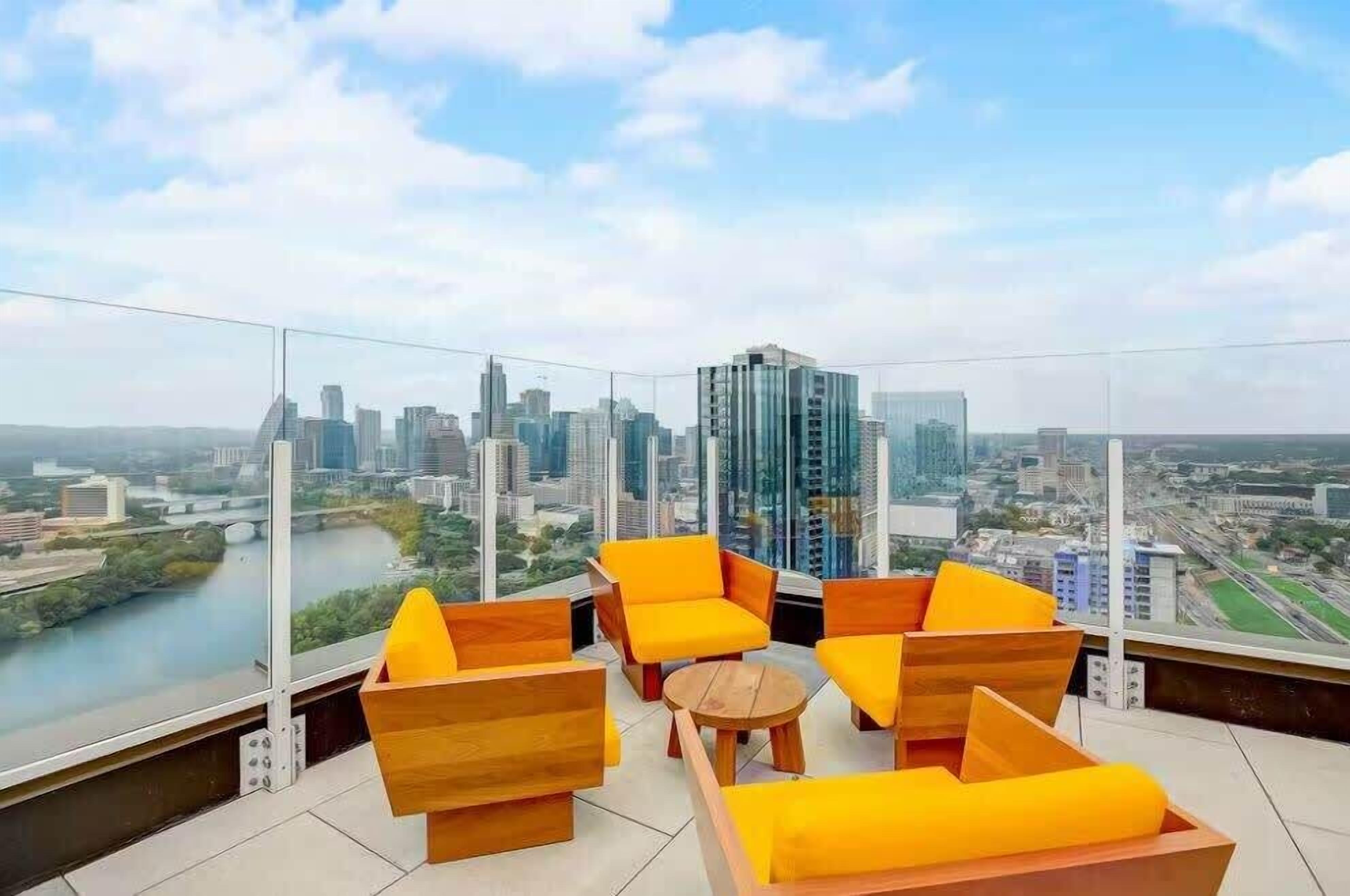 A high-rise room with a city view, featuring orange seating and a small round table.