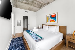 Ein Hotelzimmer mit einem Bett, einem Fernseher, einem Gemälde, einer Tür und einem kleinen Tisch.