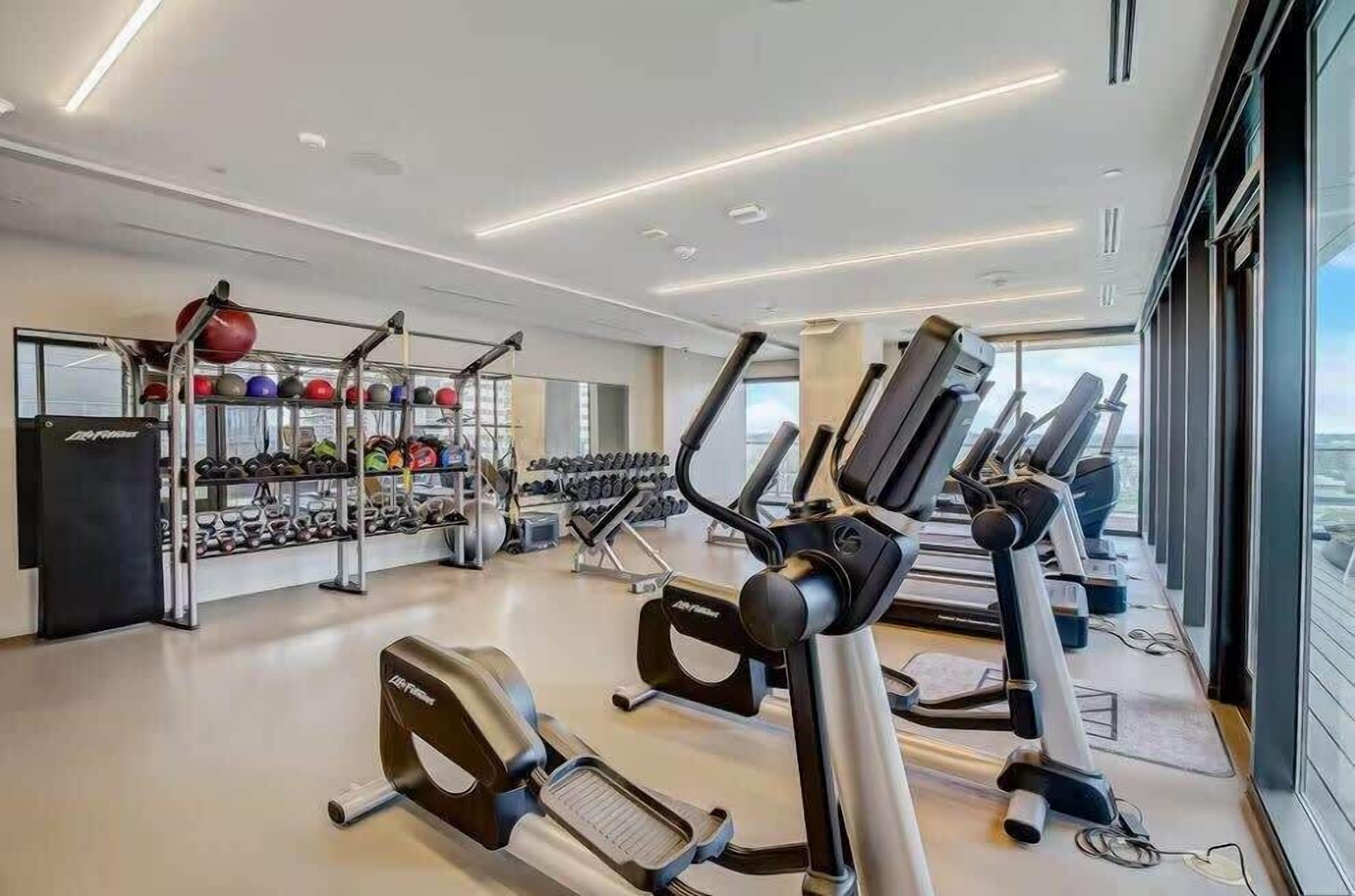A modern gym with treadmills, elliptical machines, and a variety of weights and exercise balls.