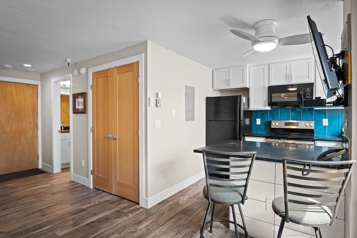 A kitchen with a black refrigerator, a microwave, and a stove. There are two bar stools and a ceiling fan.