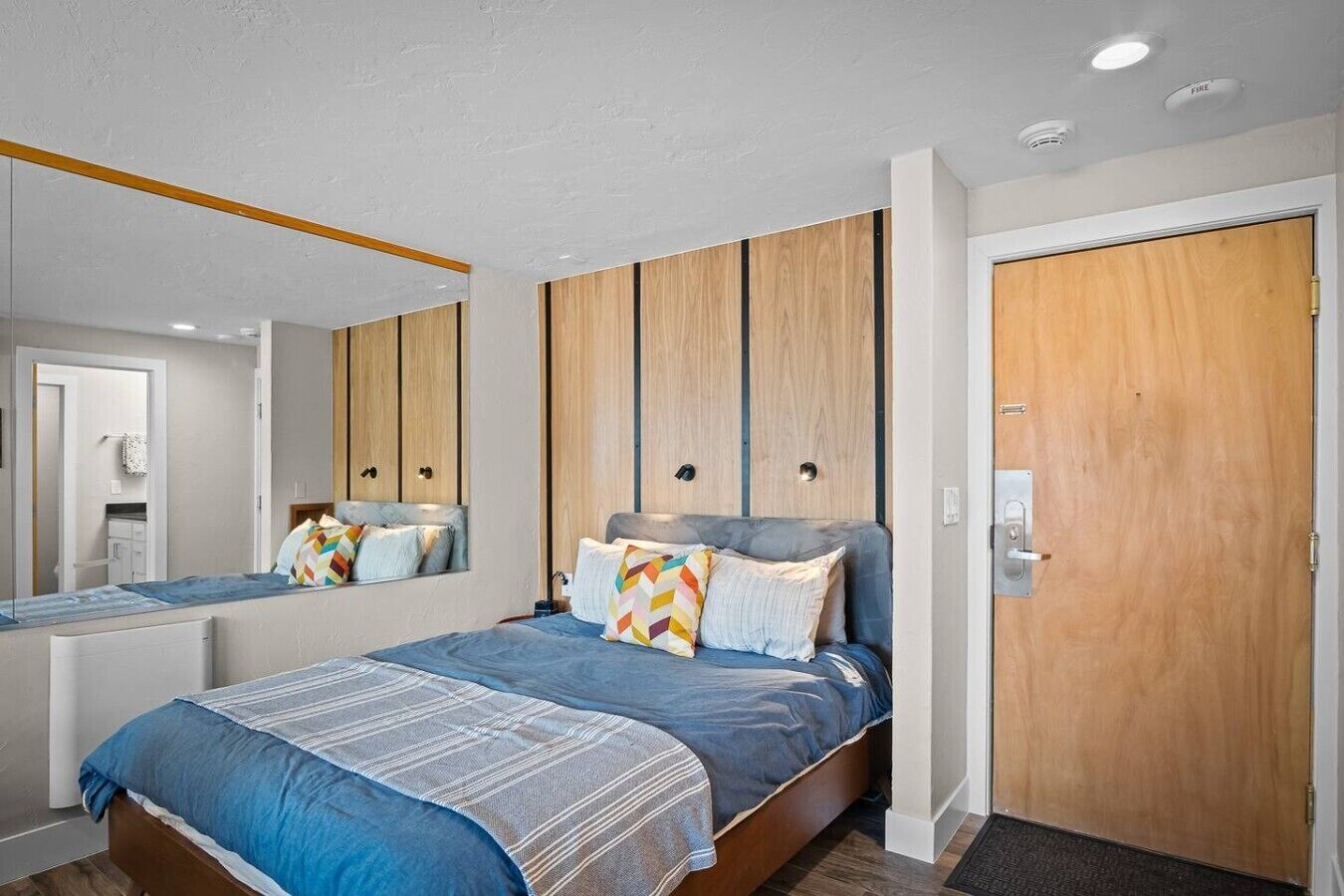 A modern bedroom with a large bed, a wooden wardrobe, a mirror, and a door.