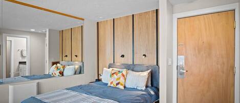 A modern bedroom with a large bed, a wooden wardrobe, a mirror, and a door.