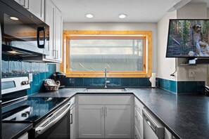 Une cuisine moderne dotée d’une grande fenêtre, d’appareils électroménagers en acier inoxydable et offrant une vue sur l’extérieur.