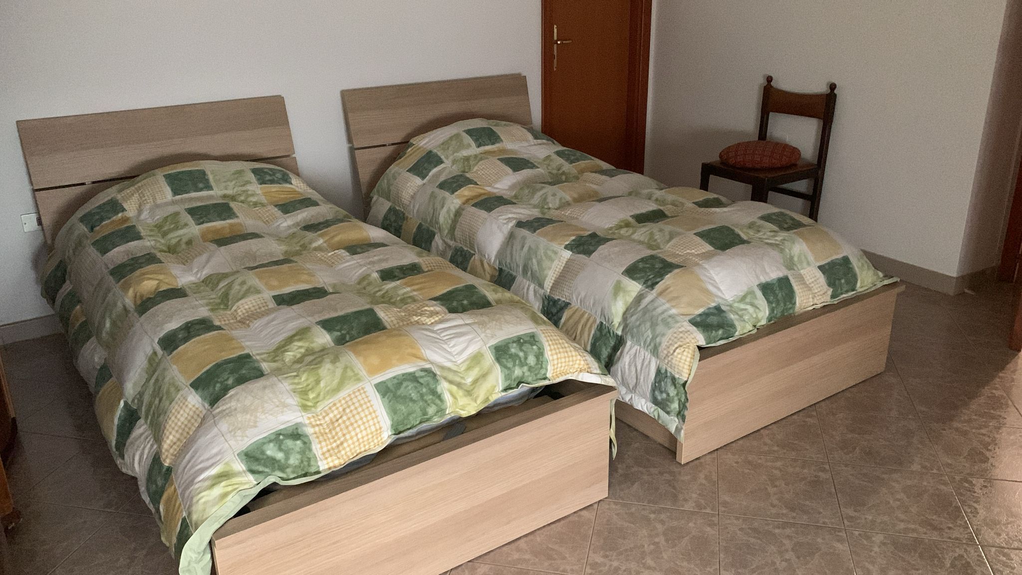 Una stanza con due letti in legno, cassettiere, una sedia e una porta.