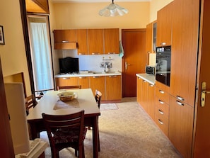 Una cocina compacta con armarios de madera, una mesa de comedor, sillas, estufa y horno empotrado.