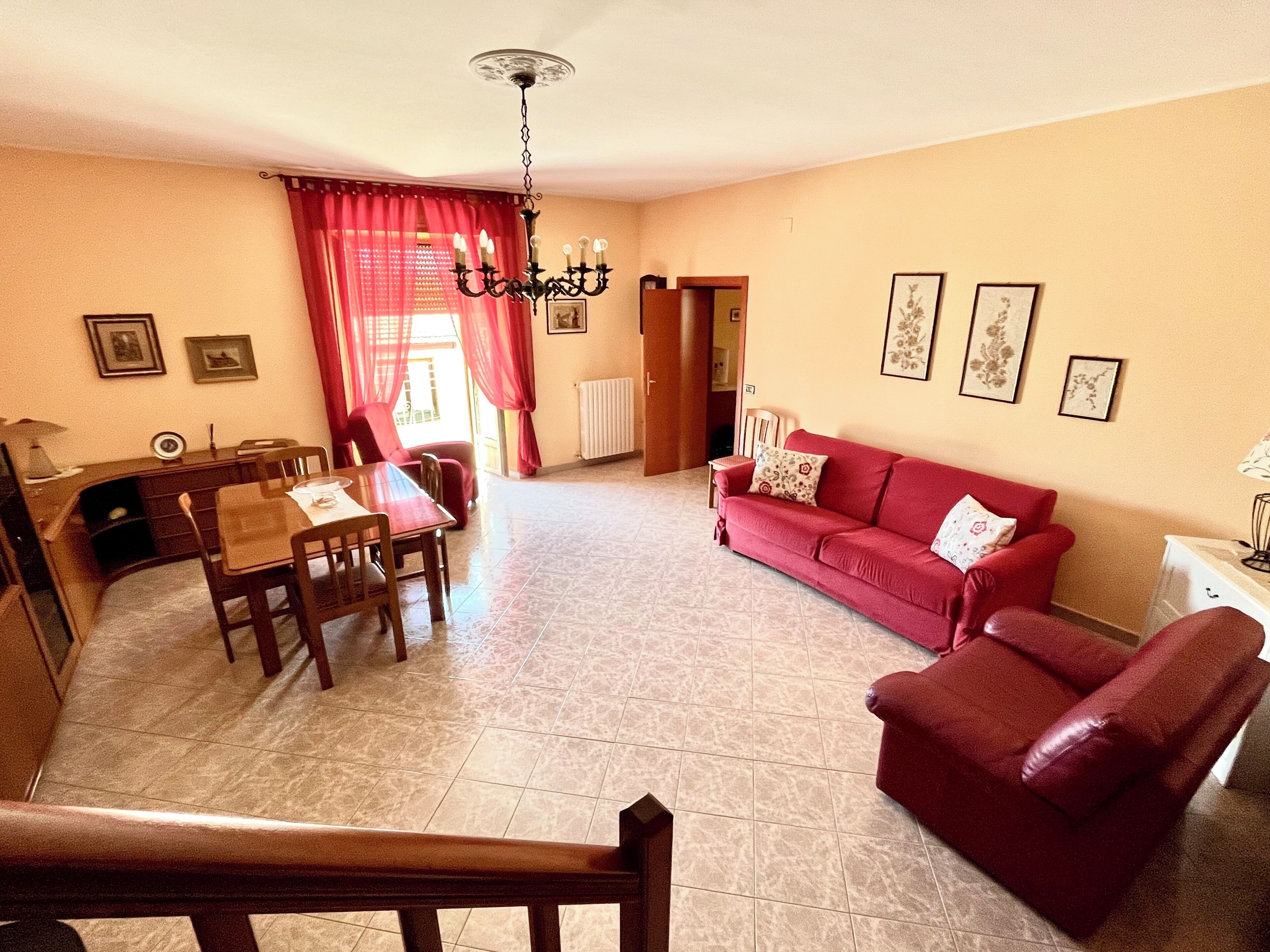 Un soggiorno con zona pranzo, arredi rossi, un lampadario e opere d'arte alle pareti.