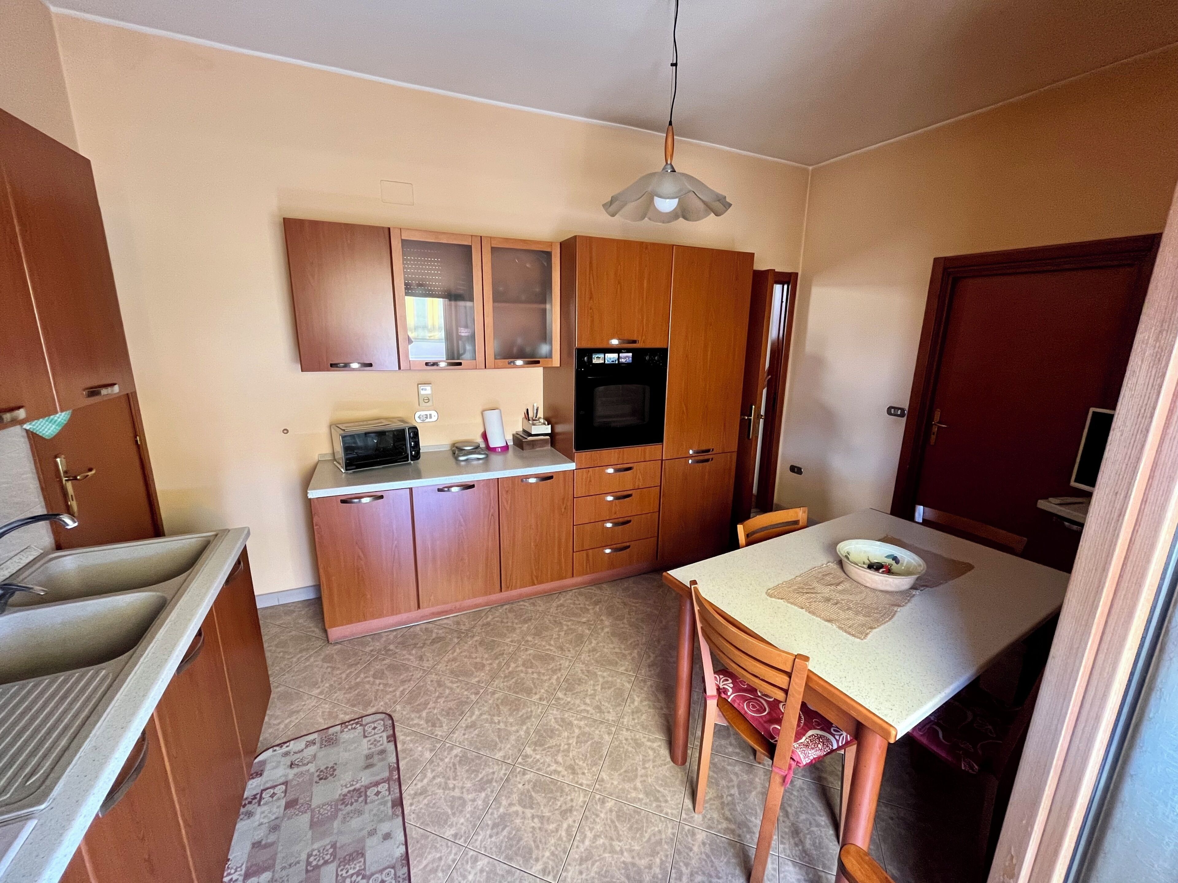 Una cucina compatta con mobili in legno, forno a incasso, microonde e tavolo con sedie.