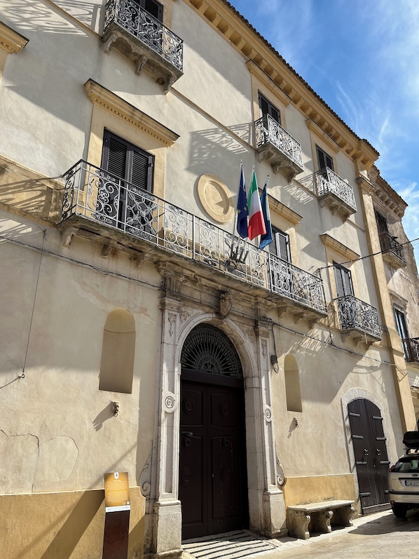 A historic building with a central entrance, ornate balconies, and flags.