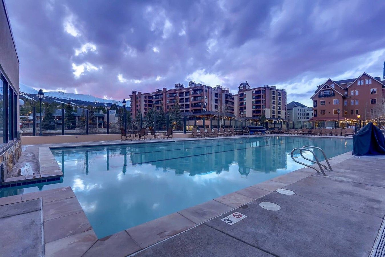 Una piscina con sillas de descanso, una zona de estar cubierta y vistas a edificios de varios pisos al fondo.