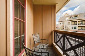 Ein Balkon mit einem Metallstuhl und einem Tisch, einer Holzwand und Blick auf Gebäude.
