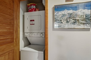 Ein Waschraum mit Waschmaschine und Trockner, einer Tüte Chips und einem gerahmten Bild einer Berglandschaft.