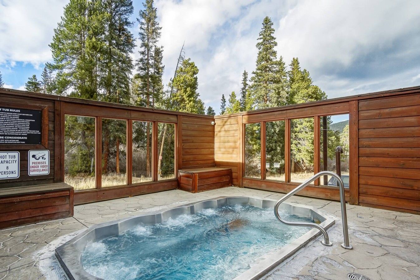 A hot tub area with a wooden deck, stone flooring, and a bench.