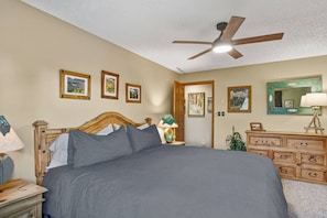 Ein Schlafzimmer mit einem großen Bett, einem Deckenventilator, einem Schminktisch und gerahmten Bildern an der Wand.