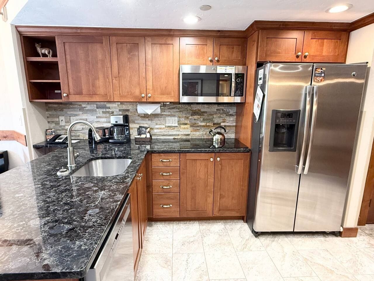Eine Küche mit Holzausstattung, einem Edelstahlkühlschrank, einer Mikrowelle und einer Arbeitsplatte aus Granit.