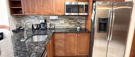 A kitchen with wooden cabinets, a stainless steel refrigerator, a microwave, and a granite countertop.