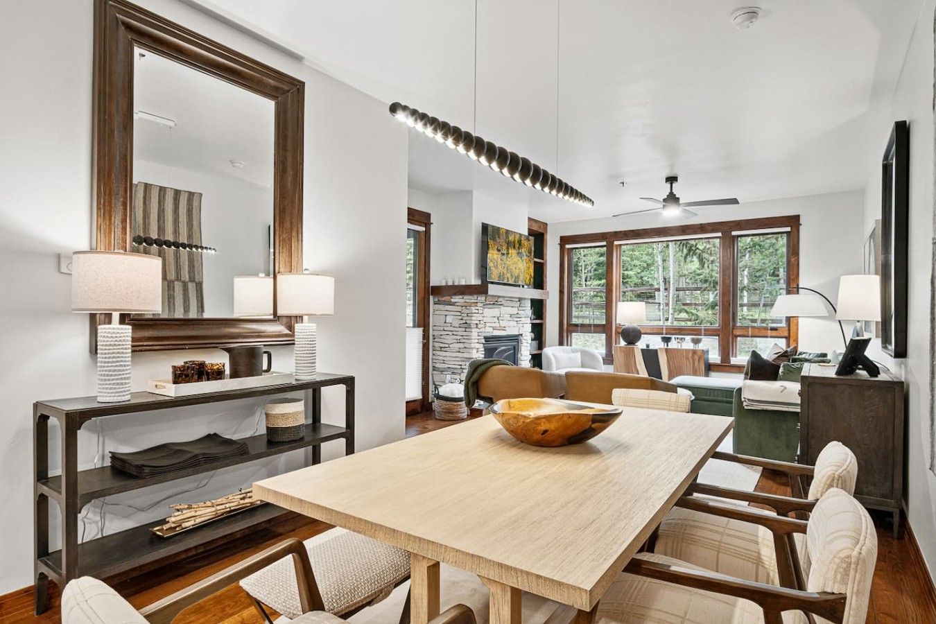 A modern living room with a dining area, large windows, a fireplace, and a ceiling fan.