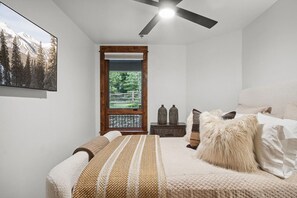 Ein Schlafzimmer mit Bett, Deckenventilator, Fenster mit Blick auf Bäume und einem Bild an der Wand.