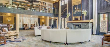 A spacious living area with a stone floor, a fireplace, and a high ceiling with wooden beams.
