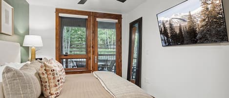 Un dormitorio con cama, almohadas, ventilador de techo, ventana y un cuadro en la pared.